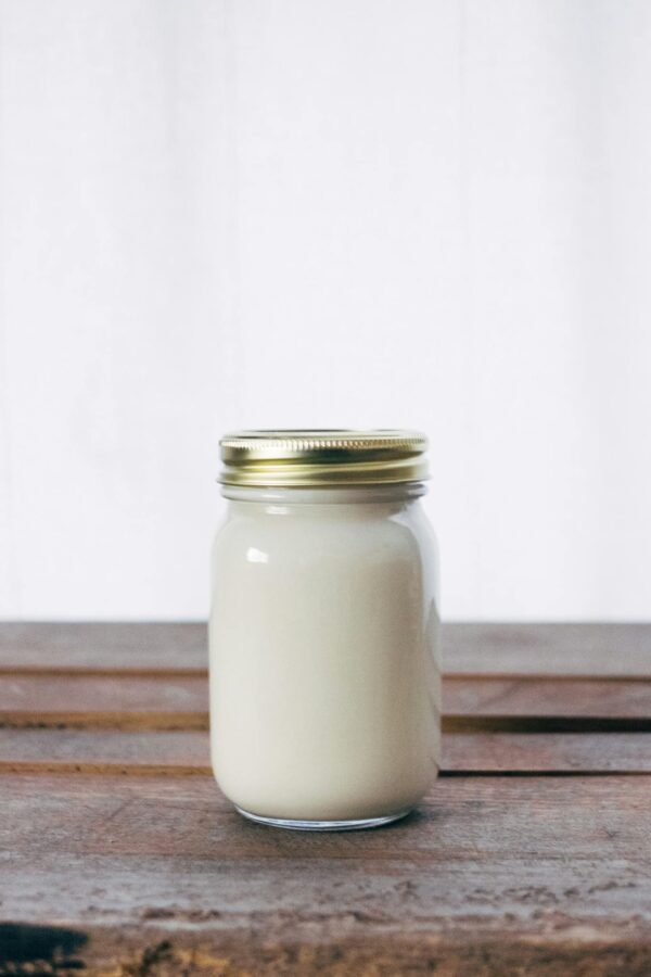 A rustic glass jar filled with creamy yogurt, placed on a wooden table. Ideal for healthy food themes.