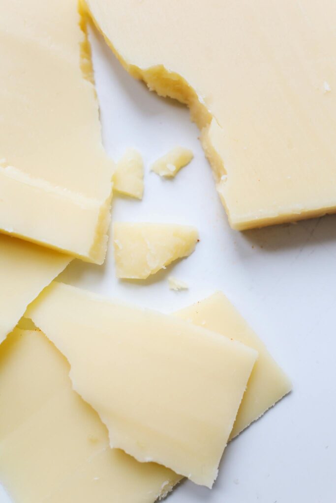 High-quality close-up image of cracked Parmesan cheese pieces on a clean white surface.